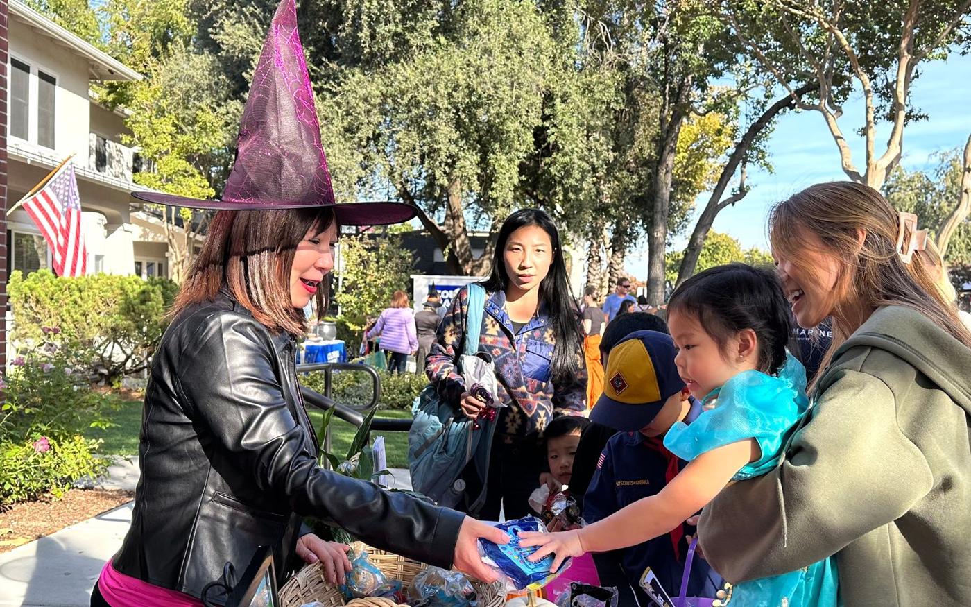 A Thriving Pink volunteer in a witch hat handing out treats to kids at a Halloween table