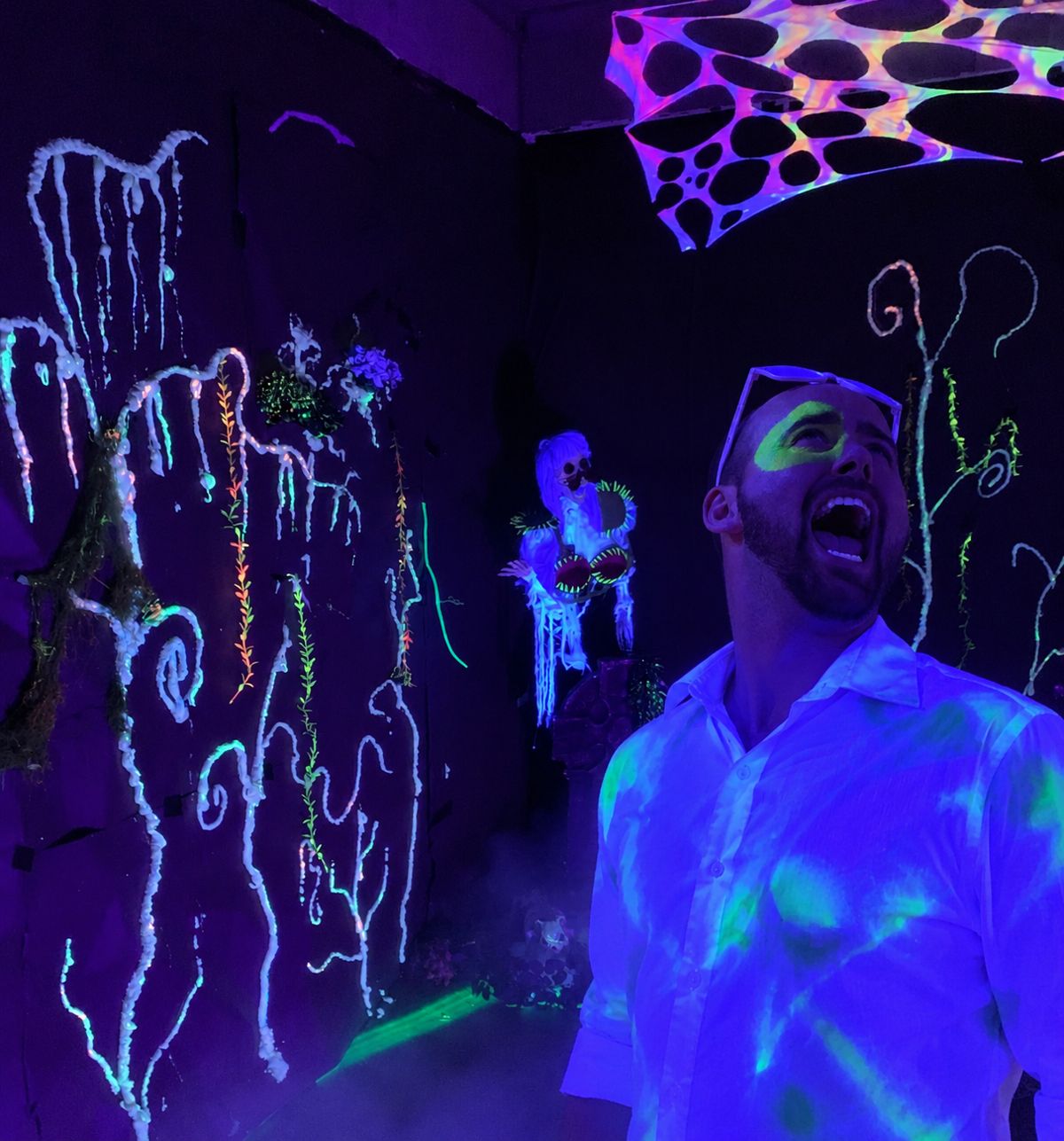 A laughing zombie in a glowing white shirt inside the blacklight forest